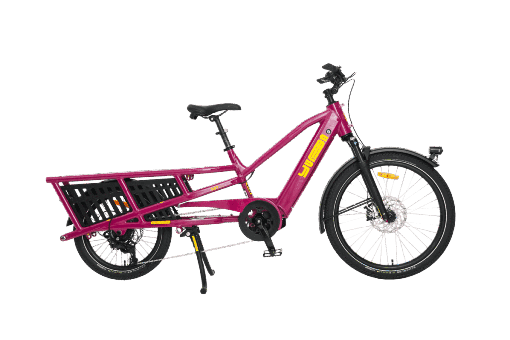 En knallrosa Yuba Spicy Curry Family Edition-lastcykel av longtail-typ med ett robust bakre pakethållare, svart sadel, stänkskärmar fram och bak samt ett stöd, utrustad med Bosch-motor, avbildas mot en vit bakgrund.