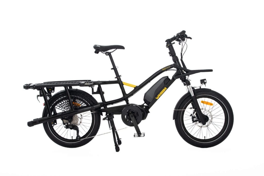 Yuba FastRack elektrisk lastcykel i svart med en kraftfull mellandriven motor, med espressofärgade accenter. Utrustad med breda däck för stabilitet, och både fram- och bakljus för säkerhet. Inkluderar ett hållbart bakre ställ utformat för att bära olika laster, vilket gör det idealiskt för att pendla eller transportera varor effektivt.