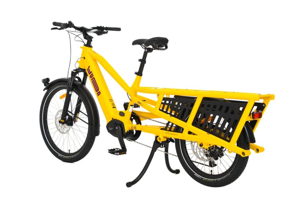 En gul eldriven lastcykel av modellen Yuba Spicy Curry Family Edition, utrustad med ett robust bakre pakethållare för transport av gods, två hjul, en ram med låg instegshöjd samt svarta detaljer på ramen och däcken. Denna eldrivna longtail-cykel är utformad för att kombinera prestanda och praktisk användbarhet.