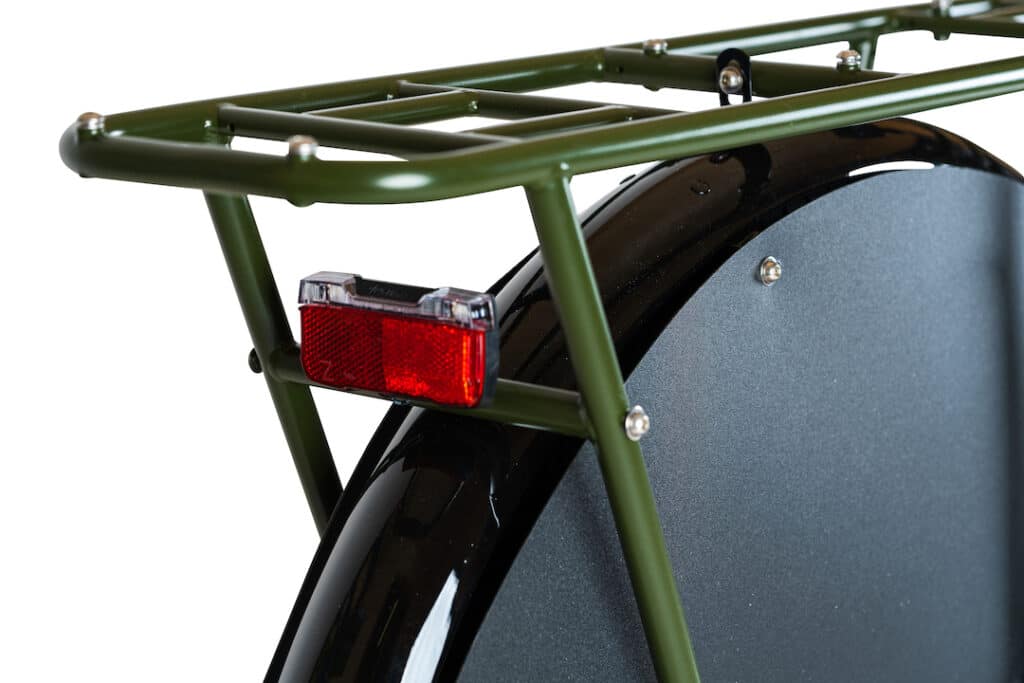 Närbild av bakdelen av en grön Yuba Mundo Lux longtail-lastcykel, med ett robust bakre pakethållare monterat ovanför en svart skärm och ett stort bakhjul, med en röd reflex fäst under pakethållaren för ökad synlighet.