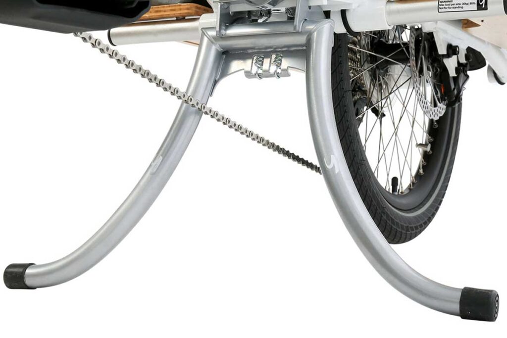 Närbild av en cykels bakhjul med en robust silverfärgad Roots Double kickstand utfälld, som håller cykeln säkert upprätt, mot en vit bakgrund.