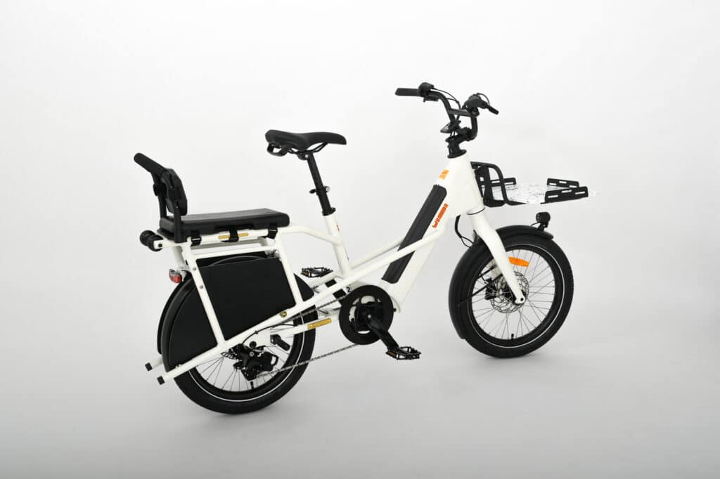 Vit Yuba Mini Boda Boda kompakt e-cargo cykel med bakre passagerarsäte, fotstöd, främre lasthållare och breda däck på vit bakgrund.