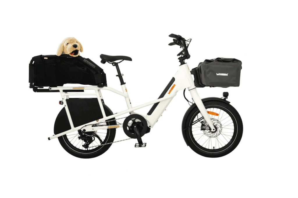 Vit Yuba Mini Boda Boda elektrisk lastcykel med svart pakethållare, hundleksak i plysch, grå styrväska, på vit bakgrund.