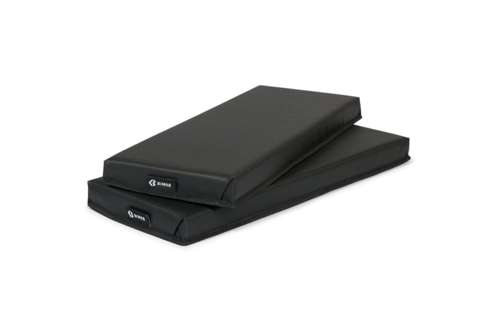 Tv&aring; rektangul&auml;ra svarta Dynor Bimas gymnastikmattor, staplade p&aring; varandra, med en liten vit GIMAX-logotyp i h&ouml;rnet, mot en vit bakgrund.