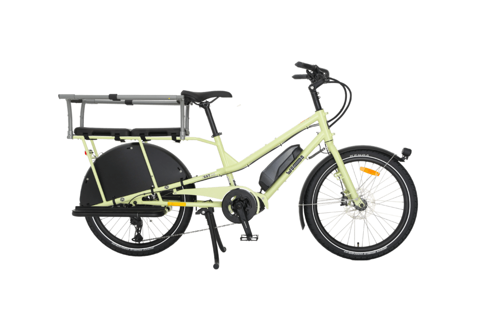 En ljusgrön eldriven lastcykel av modellen Yuba Kombi EP5 med bakre pakethållare och svarta stänkskärmar, avbildad i profil mot en vit bakgrund.
