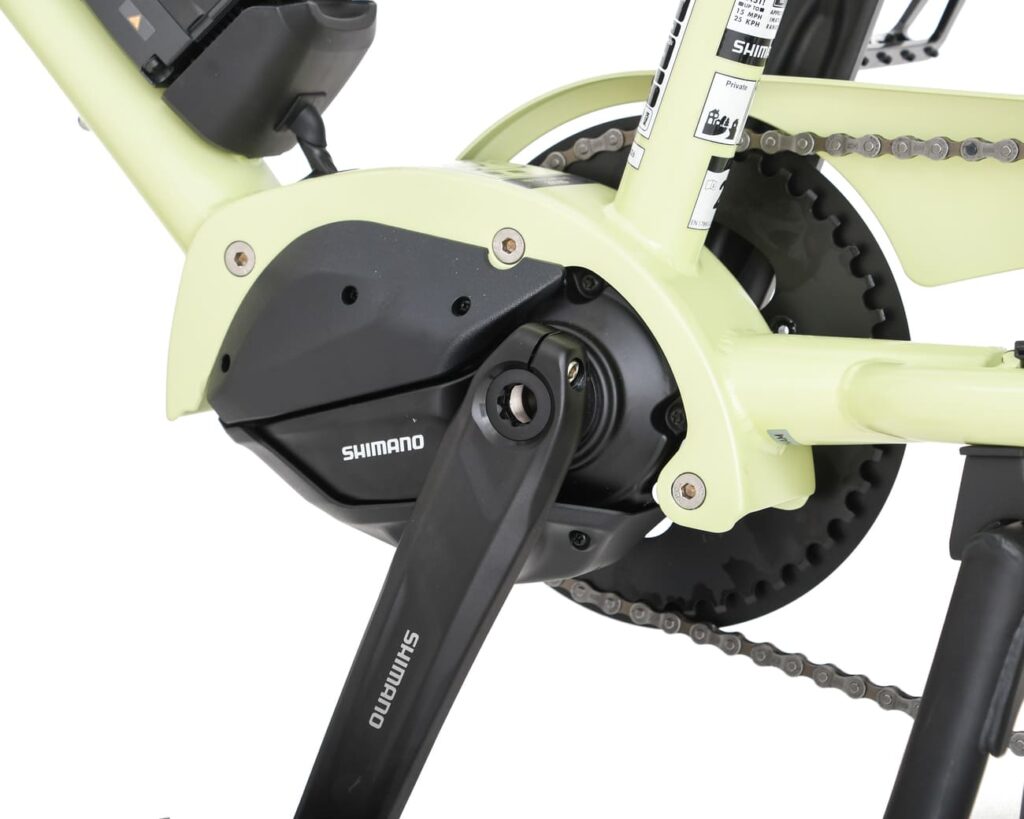 Närbild av ett Shimano-vevsats och en elmotor på en ljusgrön Yuba Kombi EP5-ram av typen longtail, där kedjan, kedjehjulet och pedalen syns i detalj.