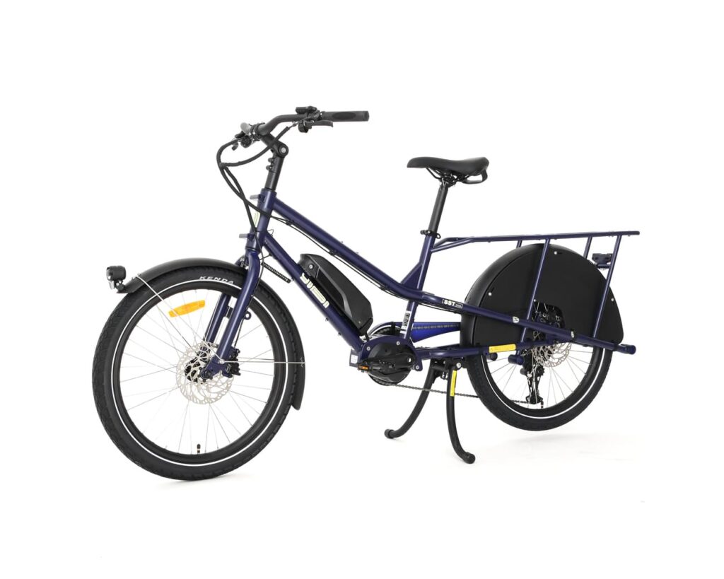 En elektrisk lastcykel av modellen Yuba Kombi EP5 i blått, med svart bakre pakethållare, framskärm och mittstöd, fotograferad mot en vit bakgrund.