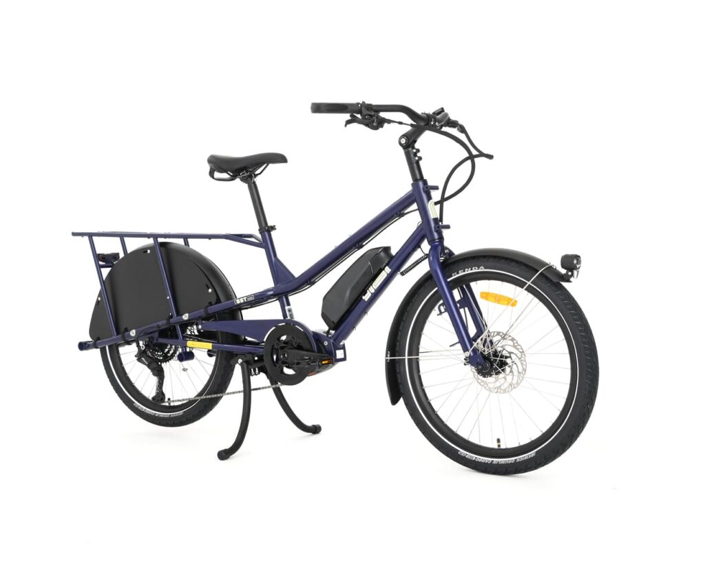 En elektrisk lastcykel av modellen Yuba Kombi EP5 i blått, med en robust ram, bakre lastkorg, svarta stänkskärmar, framljus och stödben, fotograferad mot en vit bakgrund.