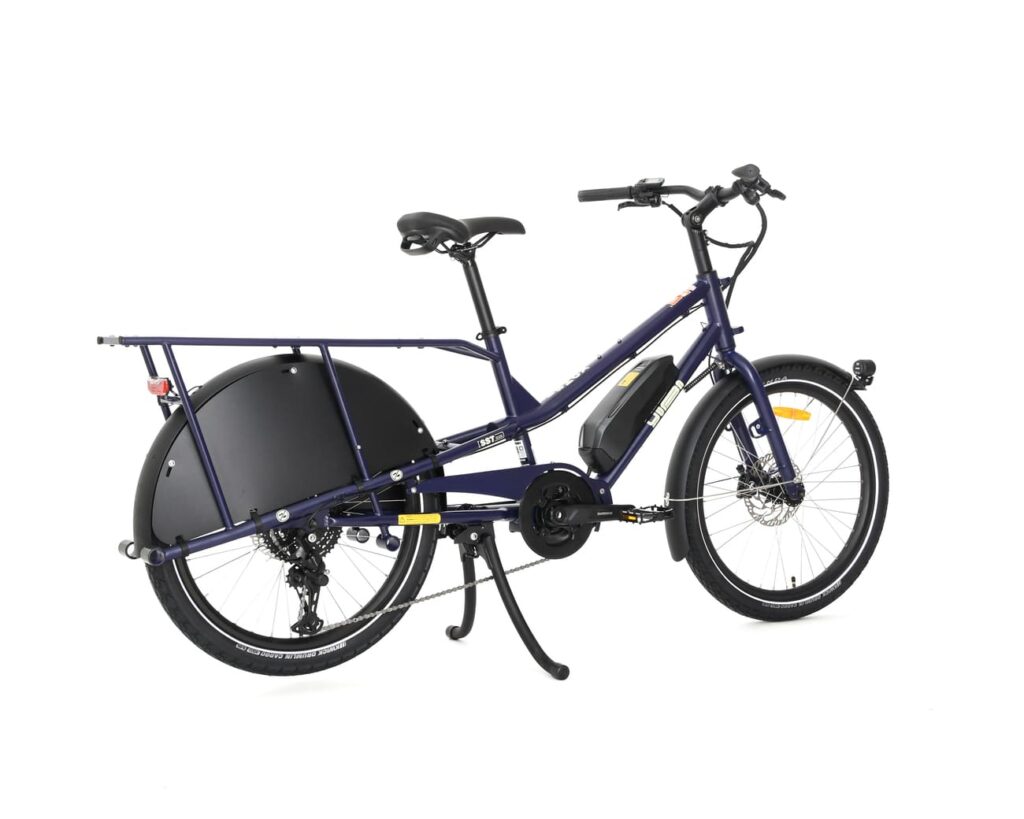 En elektrisk lastcykel av modellen Yuba Kombi EP5 i blått, med lågt insteg, stort bakre pakethållare, svarta hjulskydd och ett inbyggt batteri, visas mot en vit bakgrund.