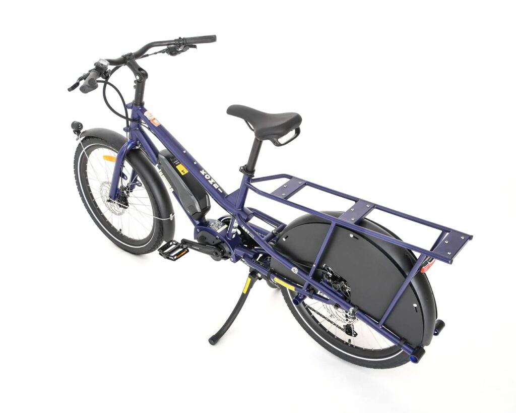 En elektrisk lastcykel av modellen Yuba Kombi EP5 i blått, utrustad med ett robust bakre pakethållare, två stora hjul, svarta stänkskärmar och ett stöd, visas mot en vit bakgrund.