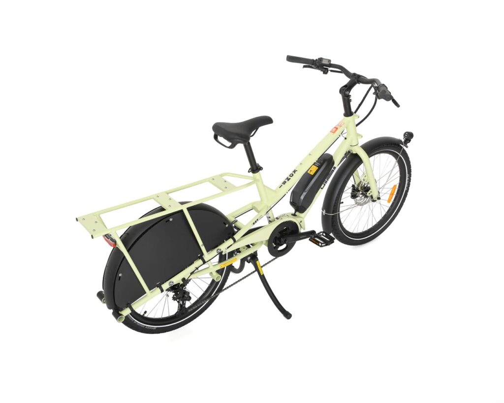 En gul Yuba Kombi EP5, en eldriven lastcykel med svart bakhjulskåpa, bakre pakethållare, stödben och ett batteri monterat mitt på ramen, avbildas från en hög vinkel mot en vit bakgrund.