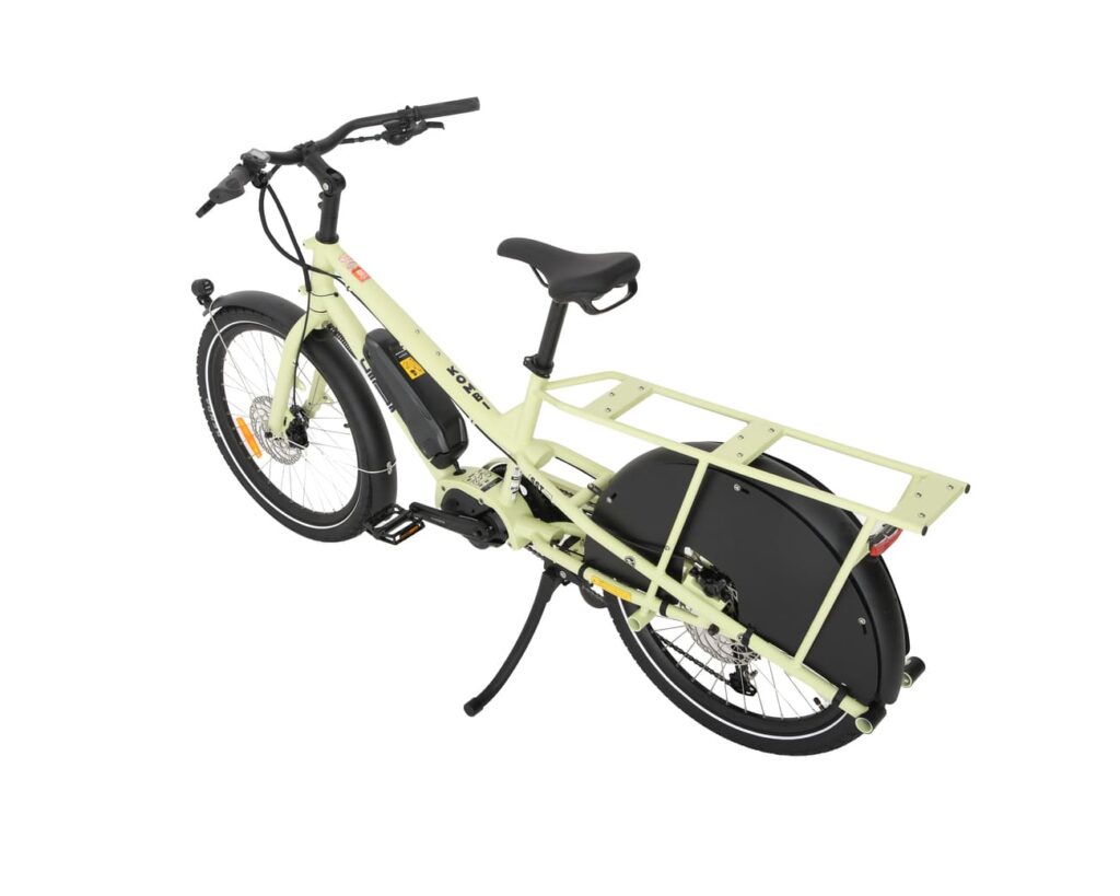En elektrisk lastcykel av modellen Yuba Kombi EP5 i ljusgrönt, utrustad med ett bakre pakethållare, svarta stänkskärmar och en svart sadel, visas från en vinkel bakifrån mot en vit bakgrund.