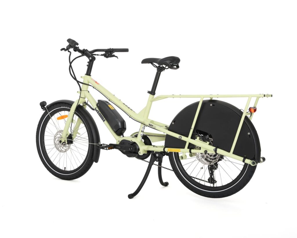Yuba Kombi EP5, som här visas i ljusgrönt och är fotograferad mot en vit bakgrund, är en eldriven lastcykel med en robust ram, bakre pakethållare, helskärmar och en elmotor integrerad vid pedalerna.