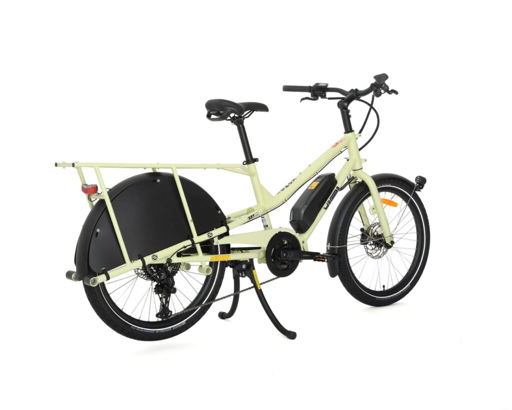 En krämfärgad Yuba Kombi EP5 visas från sidan mot en vit bakgrund, med ett svart bakhjulskydd, ett robust bakre pakethållare, ett mittstöd och ett batteri som är integrerat i ramen.