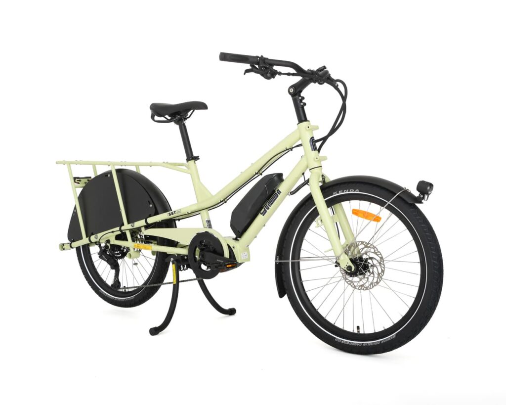 En ljusgrön eldriven lastcykel av modellen Yuba Kombi EP5, med en robust ram, ett förlängt bakre pakethållare, svarta stänkskärmar, stödben och en frammonterad strålkastare, visas mot en vit bakgrund.