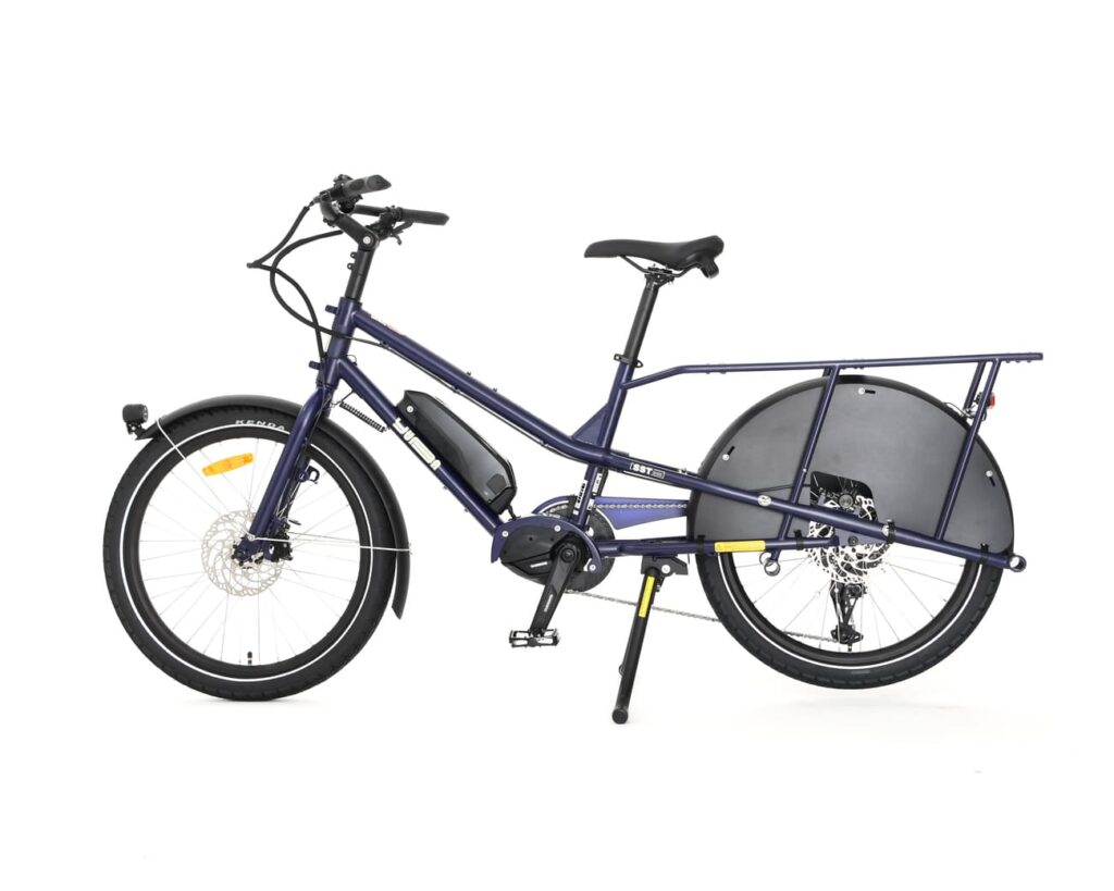 En elektrisk lastcykel av modellen Yuba Kombi EP5 i blått, med en robust ram, ett rymligt bakre pakethållare, ett batteri monterat på underröret och stänkskärmar på båda hjulen, fotograferad mot en enfärgad vit bakgrund.