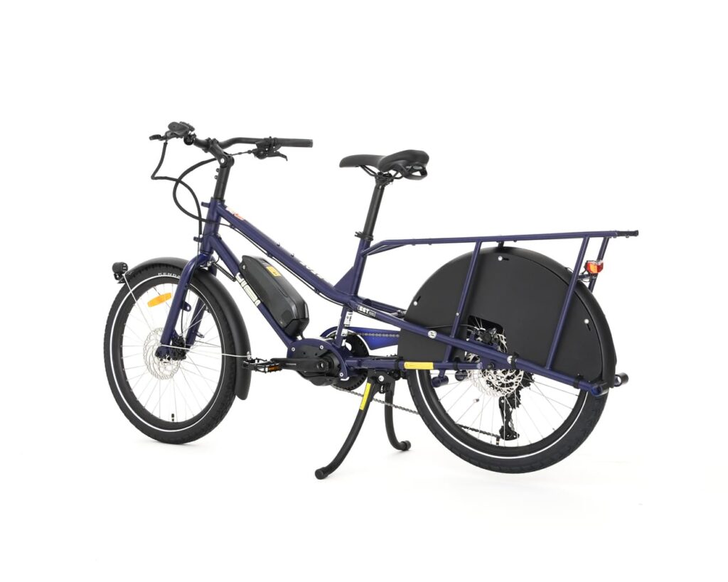 En blå Yuba Kombi EP5, en eldriven lastcykel med ett långt bakre pakethållare, dubbla stödben, ett stort kedjeskydd och en mittmonterad motor, visas mot en vit bakgrund.