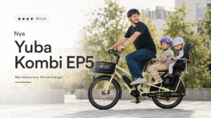 En leende man med hjälm cyklar på en ljusgrön Yuba Kombi, en eldriven lastcykel, med två små barn – som också bär hjälm – sittande bakpå. Scenen utspelar sig utomhus med träd och byggnader i bakgrunden. EP5-test pågår.